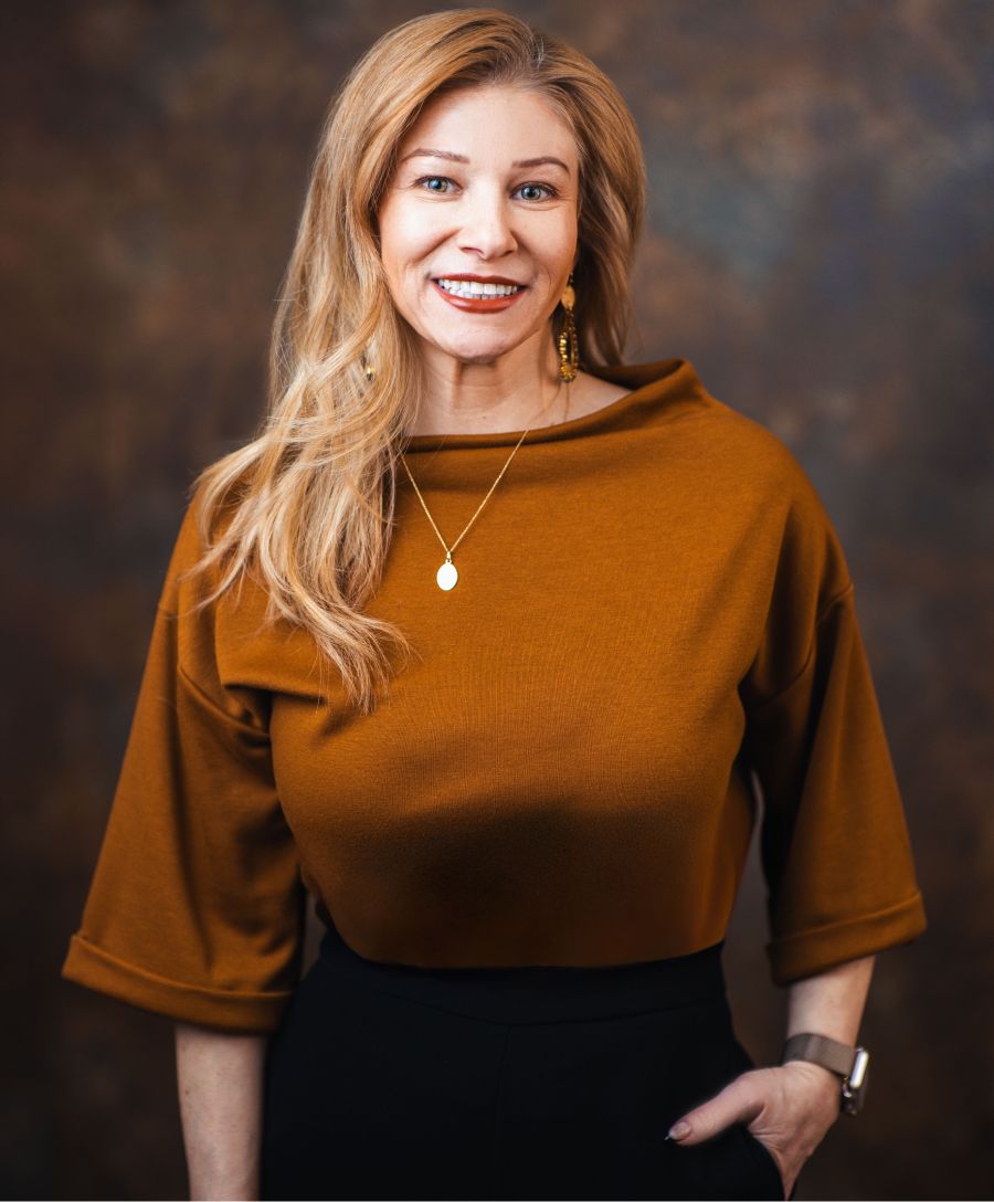 Smiling woman in amber sweater against dark background.