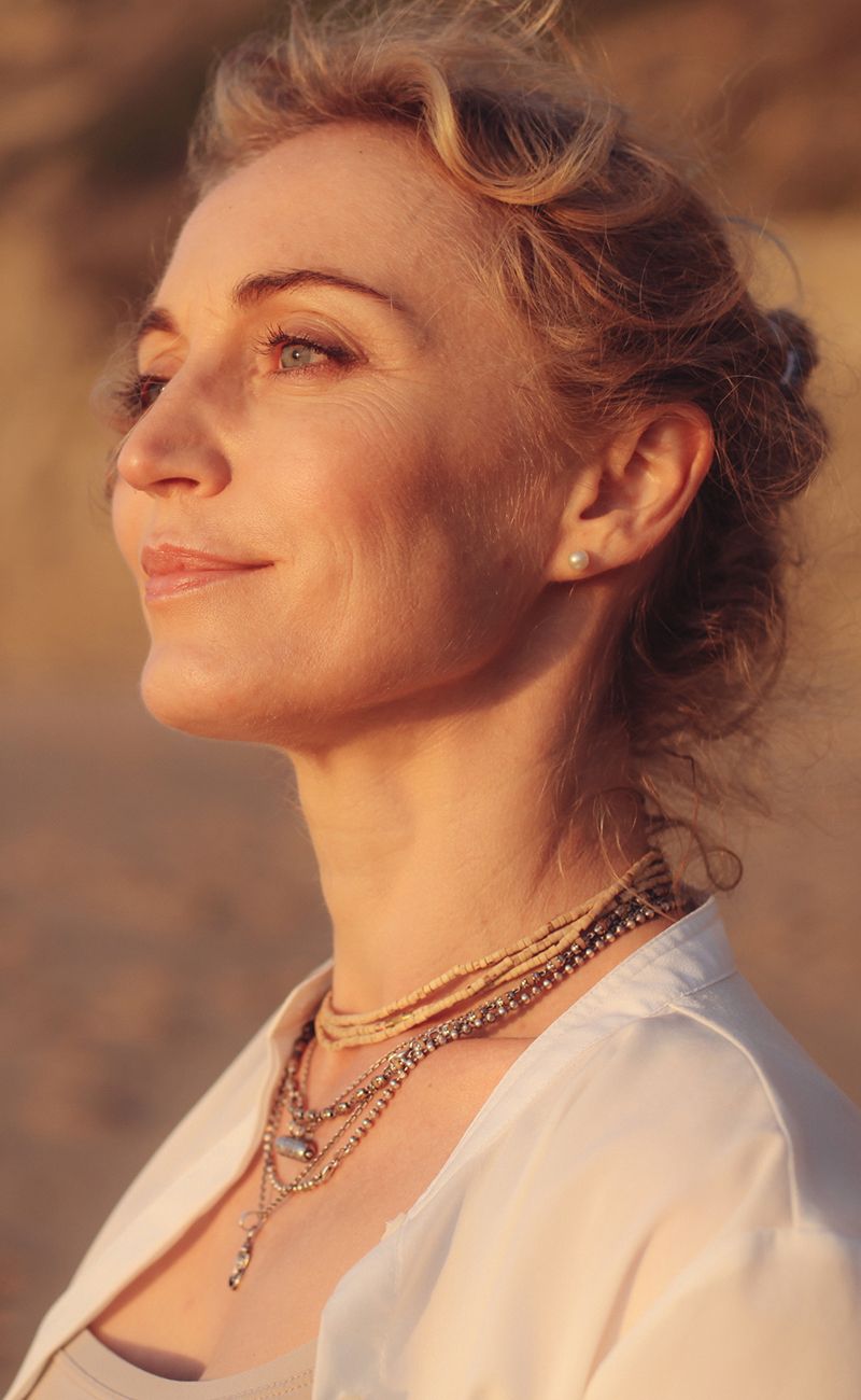 Woman with curly hair wearing layered necklaces.